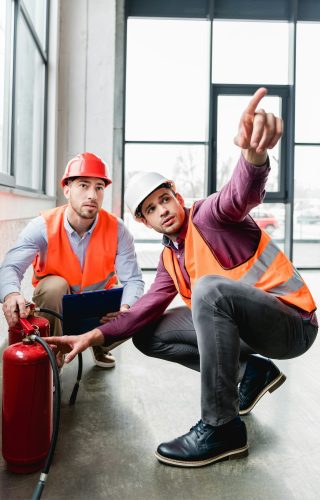 fireman pointing with finger near coworker while sitting near red extinguishers